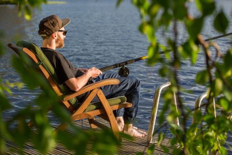 Eine Person sitzt in einem Stuhl an einem See und hat eine Angel in der Hand