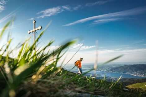 Vordergrund Gras, dahinter ein Mann der bergab geht, im Hintergrund ein See mit weiteren Bergen